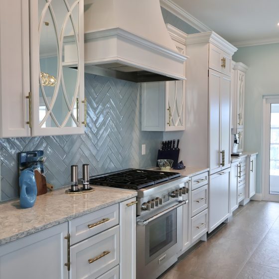 Bali Tide Remodel kitchen in Gulf Breeze, Florida featuring custom white cabinetry, paneled refrigerator and freezer, professional-style range, built-in coffee bar, and gold hardware in an open coastal floor plan.